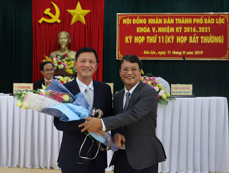 Tân Chủ tịch UBND TP Bảo Lộc Đoàn Kim Đình (bên trái) nhận hoa chúc mừng từ ông Phùng Ngọc Hạp - Chủ tịch HĐND TP Bảo Lộc khóa V