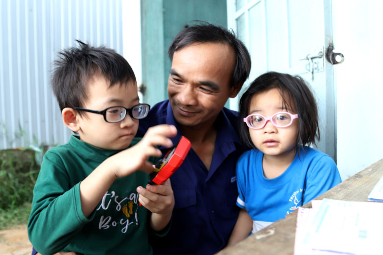 Thời gian vợ lo cơm nước, anh Hoàng chơi đùa cùng 2 cháu Trần Khánh Đăng (5 tuổi) và Trần Nguyễn Quỳnh Trâm (4 tuổi) đều bị bệnh cận thị bẩm sinh từ 14 – 16 độ, lúc nào cũng phải đeo mới có thể đi lại và luôn cần bố mẹ bên cạnh giúp đỡ