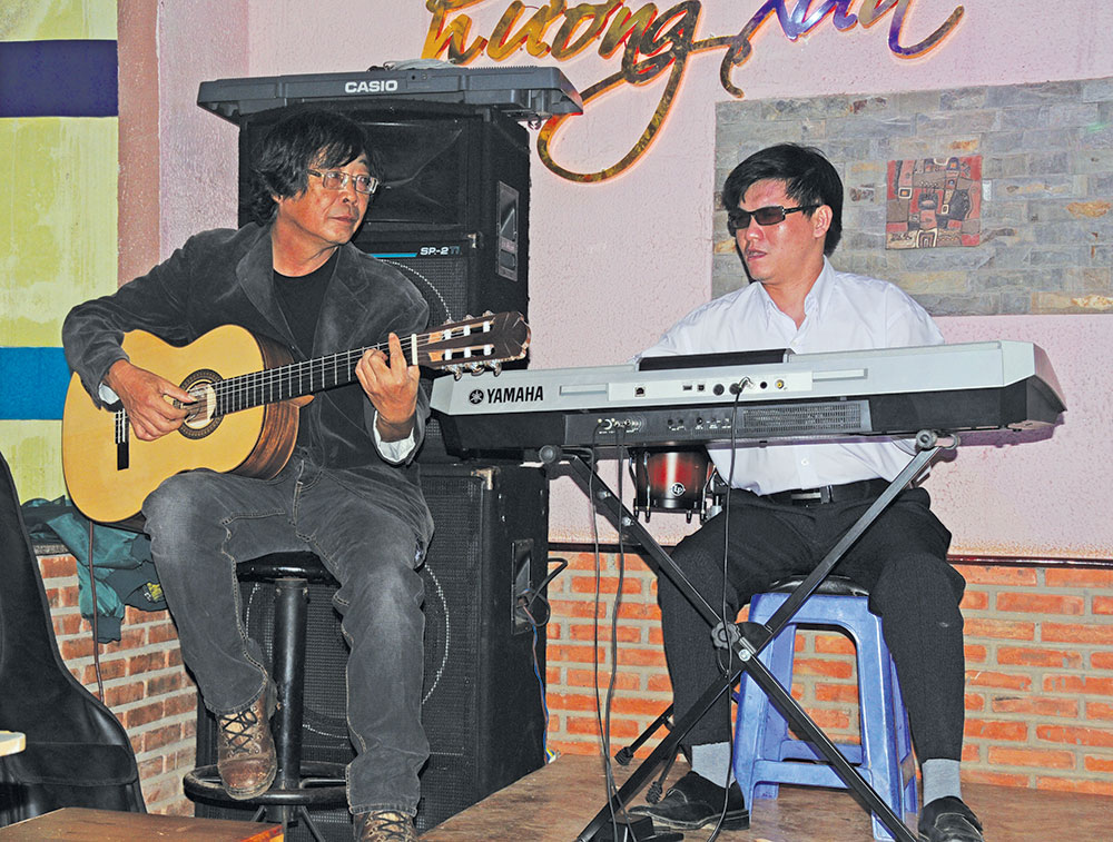 Lai làm nhạc công ở một quán cà phê vào ban đêm ở thị trấn Di Linh bên cạnh một “đồng nghiệp” Organ keyboard mù. Ảnh: N.H.T
