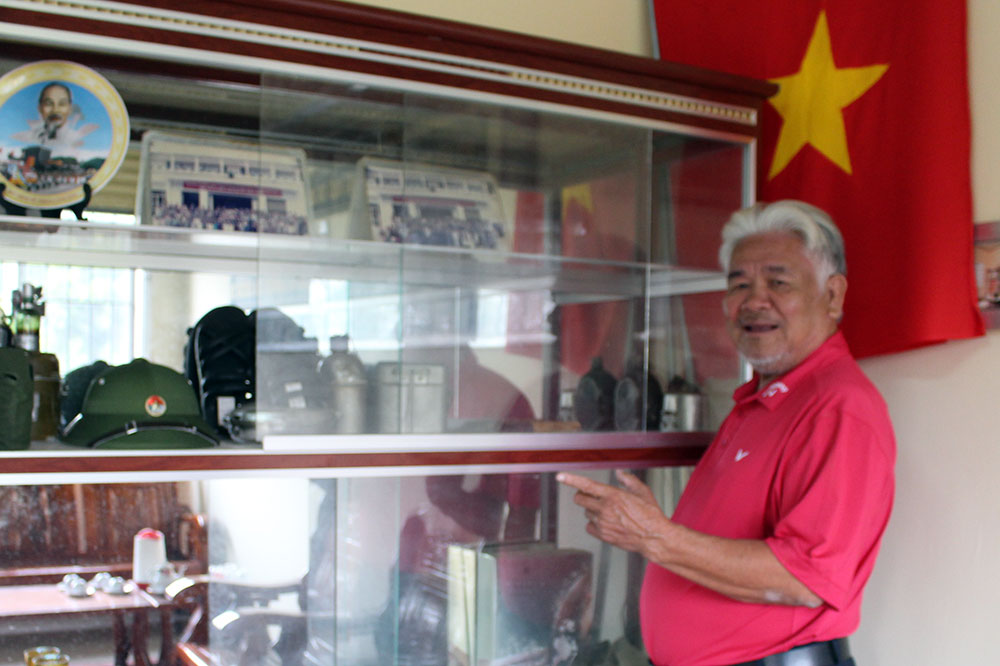 Ông Lê Đình Mai bên các vật dụng lưu niệm trưng bày tại nhà truyền thống của xã.