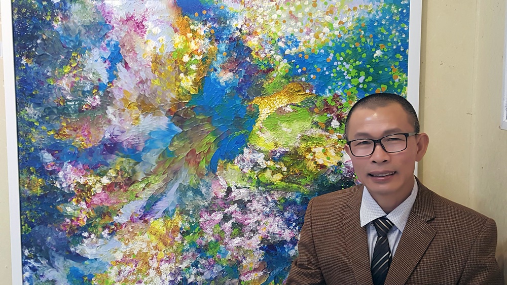 Họa sỹ Võ Trịnh Biện bên các tác phẩm mỹ thuật đang triển lãm tại Nhà Triển lãm Hòa Bình
