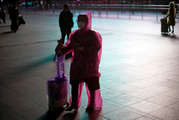 Một phụ nữ đeo khẩu trang và mặc áo mưa để bảo vệ mình tại một ga tàu ở Thượng Hải, Trung Quốc ngày 17-2
