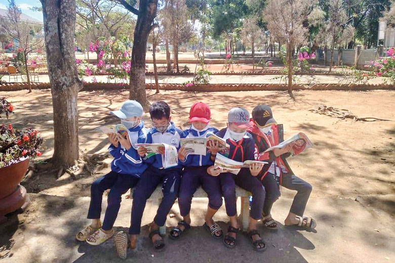 Các em học sinh say sưa đọc sách dưới tán cây tại Trường Tiểu học - THCS Tà Hine (xã Tà Hine, huyện Đức Trọng)