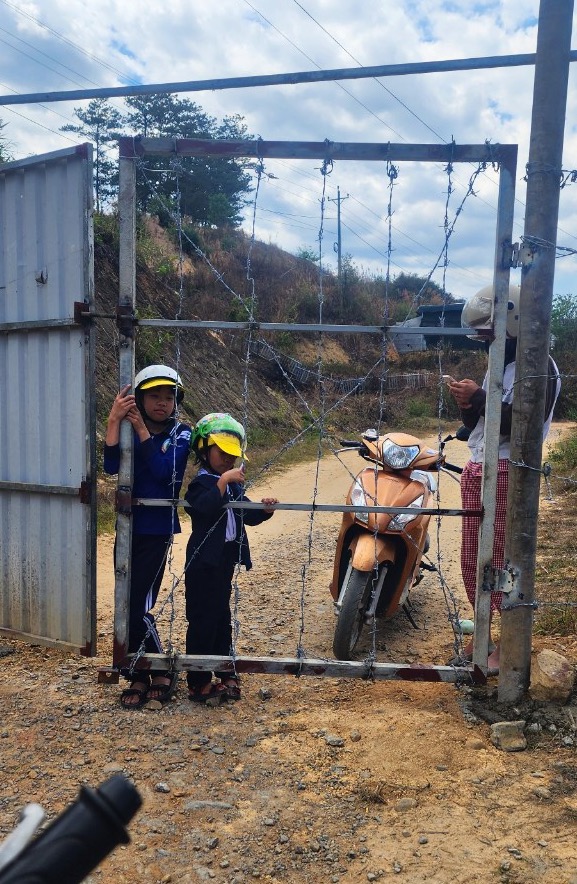 Phụ huynh và các em học sinh đợi bảo vệ ra mở cổng hàng rào. Nhiều ngày qua có nhiều phụ huynh và các em phải tự chui hàng rào để đi tới trường