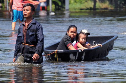 Một người đàn ông kéo hai con gái trên một chiếc thuyền qua dòng nước lũ ở Bangkok. Ảnh: AFP