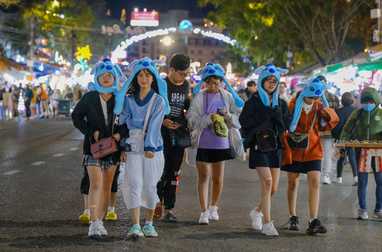 Một nhóm bạn trẻ đội khăn thỏ chống lạnh đi dạo tại chợ đêm Đà Lạt. Tuy nhiên, việc đeo khẩu trang ít được các bạn trẻ để ý, thực hiện